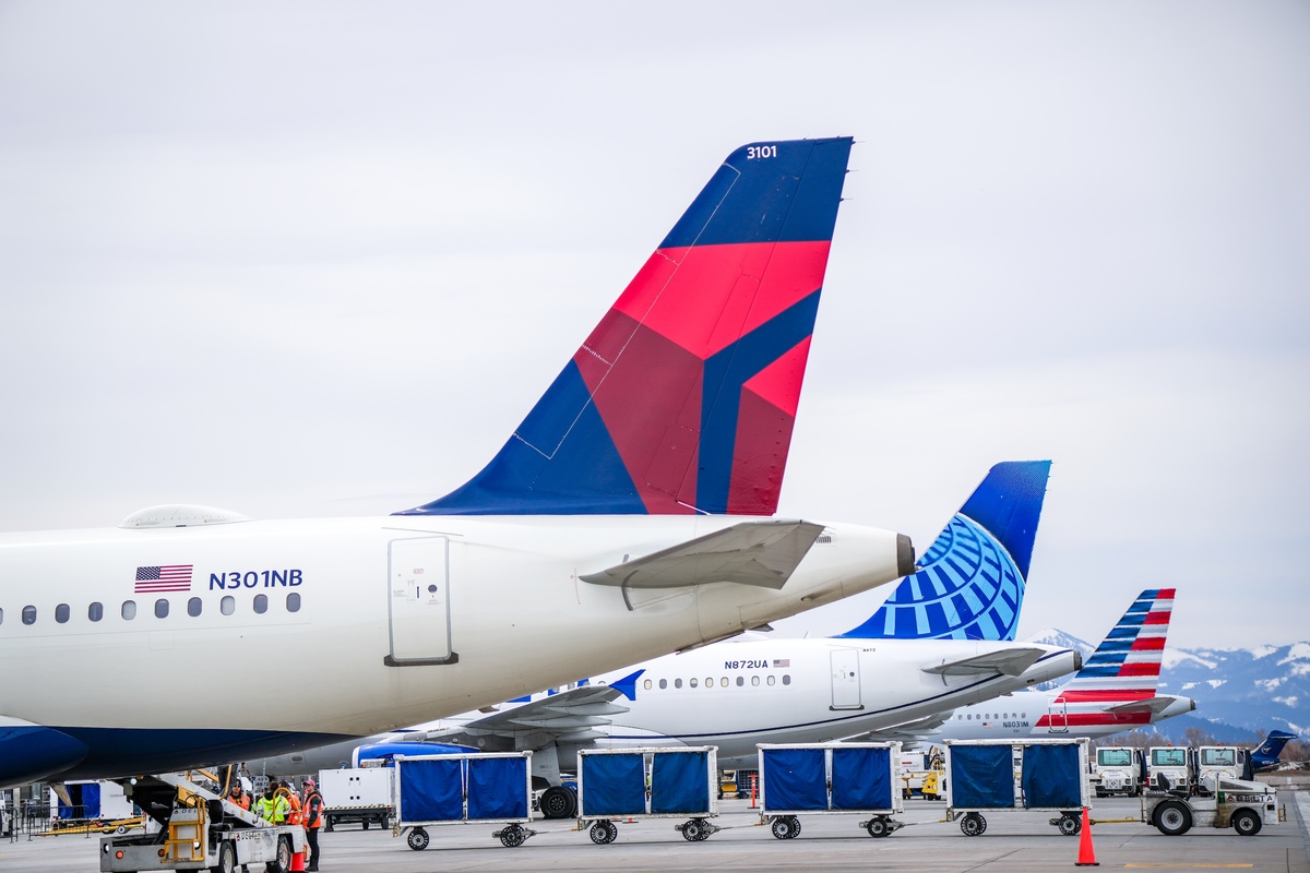 Airport scene showing three airplane tails with distinctive designs in a row on a cloudy day